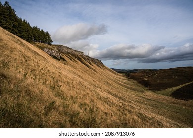 Steep grassy sloped hillside with cliffs in the distance