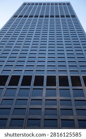 A steep low-angle view looking straight up a towering dark glass and steel corporate skyscraper.