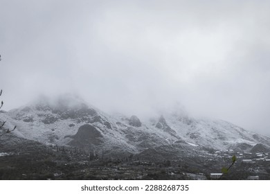 Steep rocky mountain range partially hidden by dense fog, with peaks covered in snow - Powered by Shutterstock