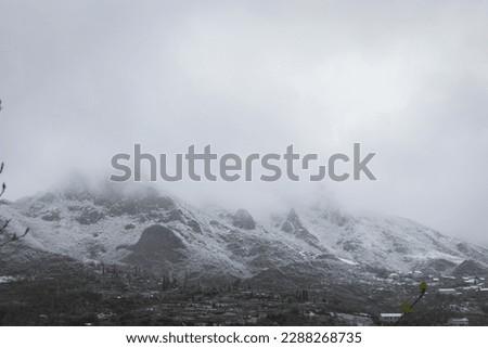 Steep rocky mountain range partially hidden by dense fog, with peaks covered in snow