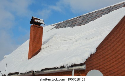 A Steep Slope Metal Roof Covered With Snow With A Chimney, Rain Gutters But Without Snow Guards In Winter. Snow Is Sliding, Falling From A Steep Metal Roof Without Snow Guards.