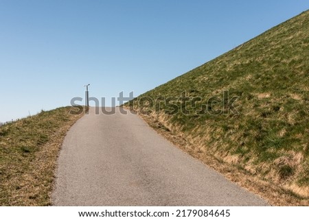 Steep uphill road with grass fields on each side.
