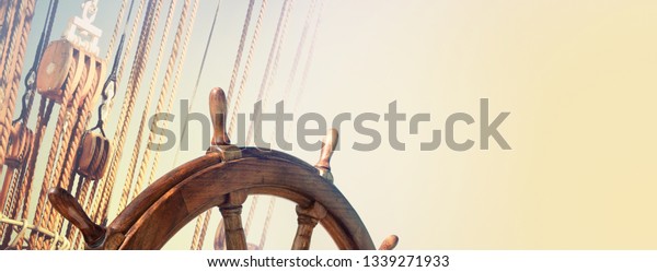 Steering wheel and marine\
ropes on the old ship for your concept of marine voyage under\
sails. Nautical equipment on ancient sailing vessel with a wooden\
wheel of captain.