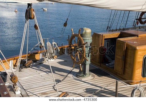 Steering wheel on\
the deck of a wood\
sailboat