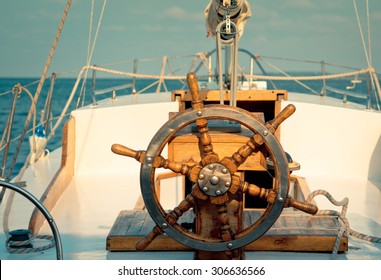 Steering Wheel On The Old Sailboat. Sea Voyage Of The Sailing Vessel. Travel At Sail Boat With A Wooden Helm In Front. Ship Wheel On The Old Yacht - Nautical Equipment Closeup.