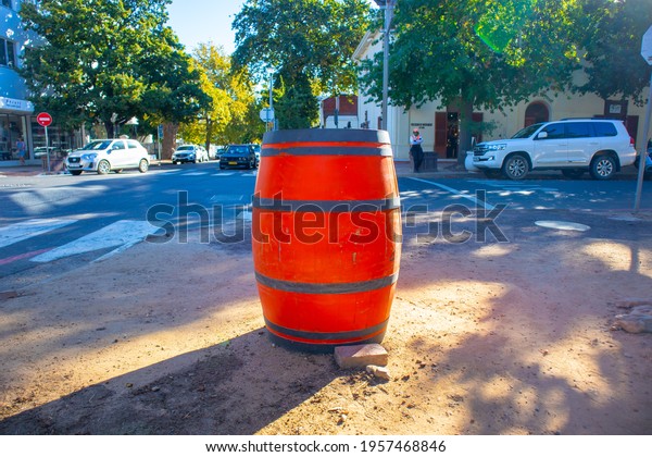 Stellenbosch, Cape Town, South\
Africa 08-04-2021\
\
Bright orange barrel standing on the road side\
in the Stellenbosch village area. Trees, buildings and cars in\
background.