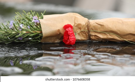 Stem Of Rosemary Wrapped In Brown Paper With A Poppy Flower On A Wet Stone Surface For Anzac Day Commemoration Ceremony Service. Lest We Forget. Dawn Service. Veterans And Ex Servicemen. Allied Forces