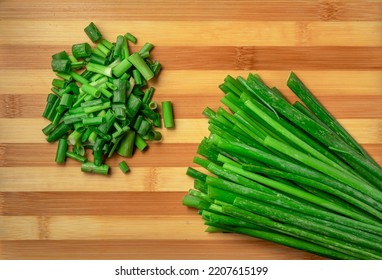 Stems and chopped pieces of fresh green onions on striped wooden kitchen board. Juicy chopped green scallion or chives slices and stalks. Greenery, seasoning for cooking fresh healthy salad. Close up.