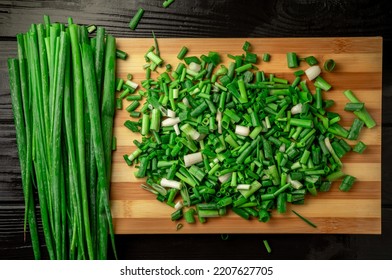 Stems And Chopped Pieces Of Fresh Green Onions On A Striped Wooden Kitchen Board. Juicy Chopped Green Scallion Or Chives Slices And Stalks On Dark Gray Wooden Table. Close Up.