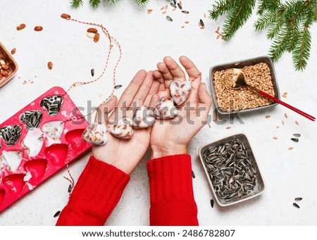 Step 7. Top view of child hands with a heart bar shaped homemade birdseed cake made from birdseeds, nuts and coconut fat. Help people to animals.