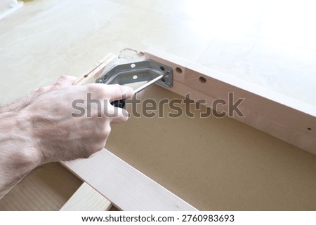 Step of assembling flat pack furniture with screwdriver and metal bracket. Home repair and installation concept.