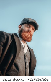 Step back in time with this captivating portrait of a gentleman dressed in the fashion of the 1920s. Complete with a stylish hat and well-groomed beard,  blue eyes and pensive expression.