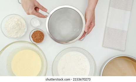 Step by step baking process. Woman using a colander over mixing bowl to sift flour and cocoa powder. Chocolate cake recipe, flat lay, copy space