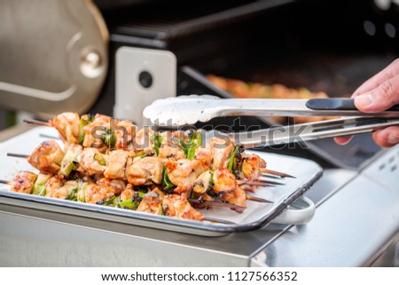 Step by step. Chicken yakitori on a white metal serving tray next to outdoor gas grill.