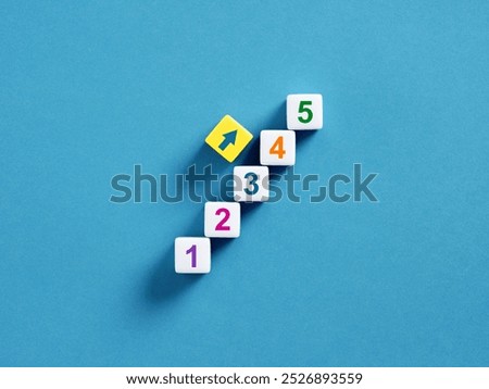 Step by step concept. Career development, accomplishing the necessary steps. Five numbered cubes arranged in ascending order forming upward steps with yellow arrow cube on top.