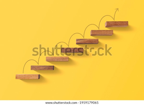 Step by step to grow your business,\
business success or career path success concept. Wooden blocks\
arranged in a shape of staircase on yellow\
background.
