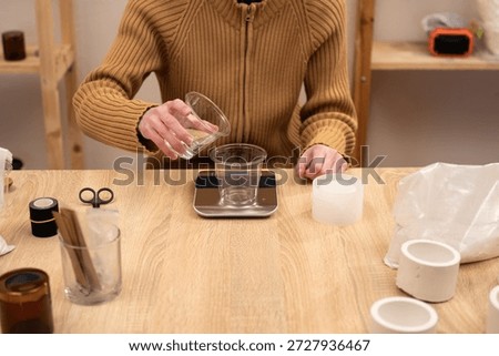 Step by step process of making a handmade gypsum candlestick: a craftsman carefully pours water into a plastic cup on electronic scales to maintain precise proportions for the mixture