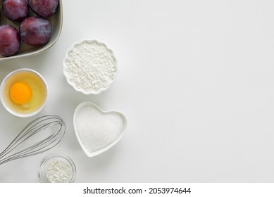 Step by step recipe for baking sweet plum pie. Ingredients set for cooking. Flour, eggs, sugar, plums for sweet pastries on white background. Top view, copy space. Culinary light background. 