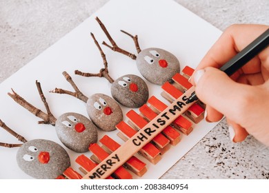 Step By Step. Top View. Process Kid Children Craft. Do It Yourself Diy Merry Christmas Deer On Greeting Card Postcard Made Of Pebbles, Sea Stones, Clothespins And Branches On White Background. Natural