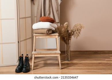 Step stool with stack of warm clothes, boots and vase in hall