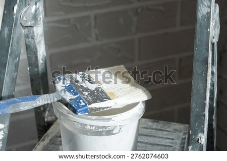 Stepladder with paint bucket and roller, ongoing wall painting, interior finishing, home repair tools, room decoration preparation, surface job.
