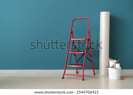 Stepladder with roll of bubble wrap, cans of paint and brushes near blue wall