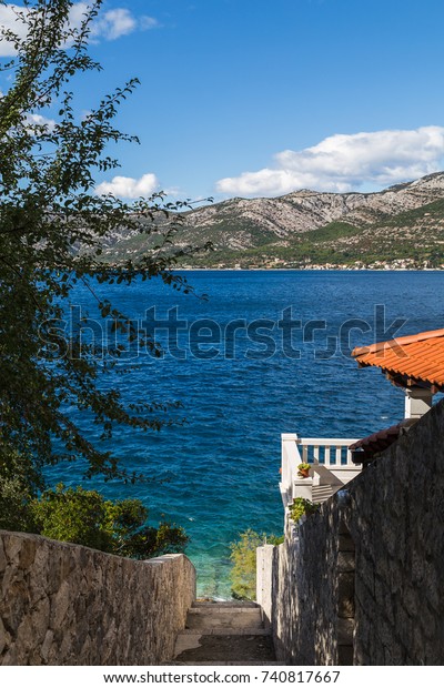 A\
stepped pathway leads down from a road towards the clear waters of\
the Peljesac channel in Croatia, a thin channel of water which\
divides Korcula Island from the Peljesac\
peninsula.
