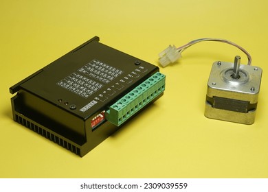 Stepper motor driver module for CNC machine with black case, green cable terminal and aluminium heat sink. 5 ampere driver with black and silver Nema 17 on yellow background isolated.
