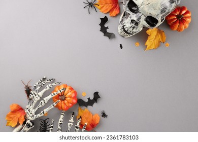 Stepping into the realm of Halloween's mysterious charm. Top view shot of skeleton hands, scary skull, colorful pumpkins, creepy decor, autumn leaves on grey background with ad zone