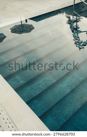 Steps leading down to a pool with blue water and reflections of umbrellas during summer vacation.