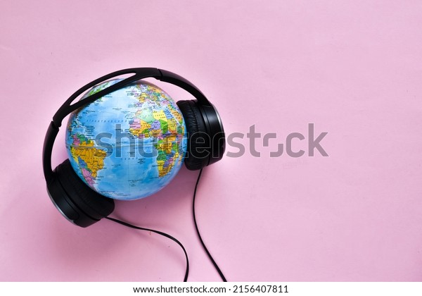 Stereo headphone and a\
globe on a pink background. World music day concept. Top view. Copy\
space