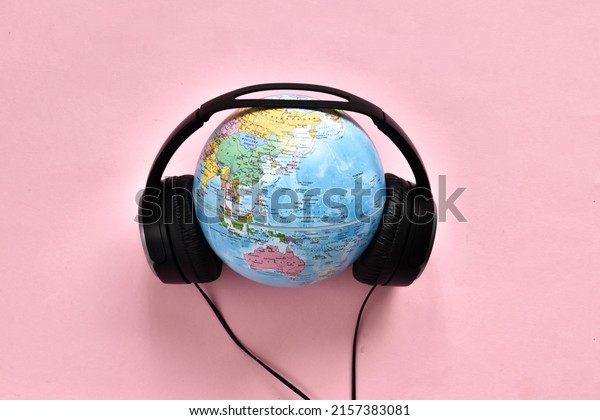Stereo headphone and a\
globe on a pink background. World music day concept. Top view. Copy\
space.