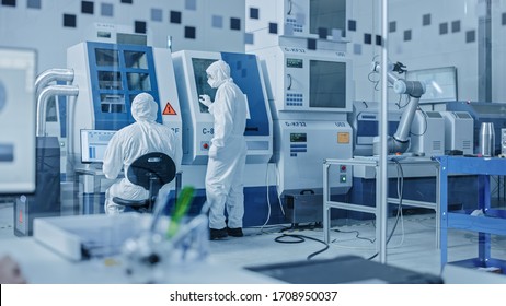 Sterile Modern Factory: Professionals in Coveralls, Masks Working on CNC Machinery. Medical Electronics Manufacturing Laboratory with High Tech Robot Arm Production Line and Contemporary Equipment