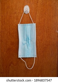 Sterile Unused Blue Face Mask Hanging From A Brown Wooden Door Isolated No People.