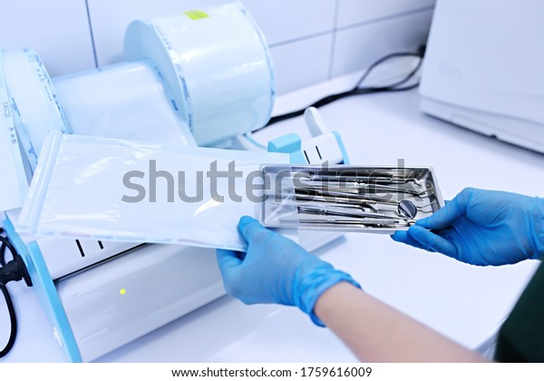 Sterilizing box. Sterilization of instruments.\
Dentist tools. Sterilization procedure. Hands in blue gloves\
holding dentist\
tools.