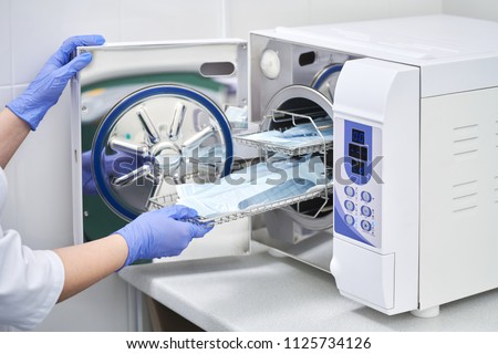 Sterilizing medical instruments in autoclave. Dental office. Dentist assistant's hands get out sterilizing medical instruments from autoclave. Selective focus. Sterile dental tools

