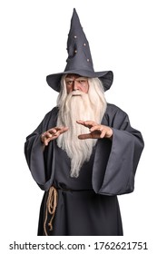 A stern grey-haired bearded wizard in a gray cassock and a cap is practicing sorcery and doing magic against a white insulating background. - Shutterstock ID 1762621751