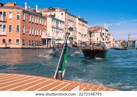 The stern of a sea cab on Venice's Grand Canal against a blurry background of blue sky, vintage houses, boats and gondolas on a sunny day, the traffic on Venice's main street, the sights of Italy