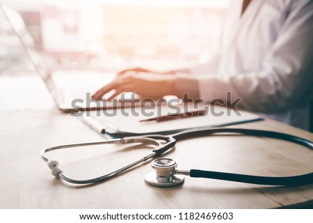 Stethoscope and background doctor using laptop at desk in clinic working on computer at room office.