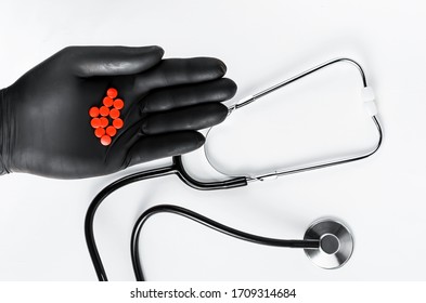 Stethoscope And In Black Medical Glove Holding Red Pills On White Background. Overhead