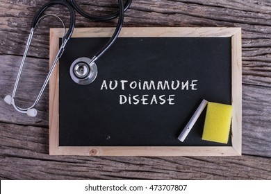 Stethoscope and Chalk board with inscription autoimmune disease on wooden background. Medical concept