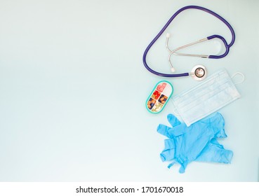 Stethoscope And Disposable Medical Mask And Nitrile Medical Gloves, Box Of Pills On A Blue Background, Top View