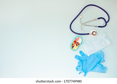 Stethoscope And Disposable Medical Mask And Nitrile Medical Gloves, Box Of Pills On A Blue Background, Top View