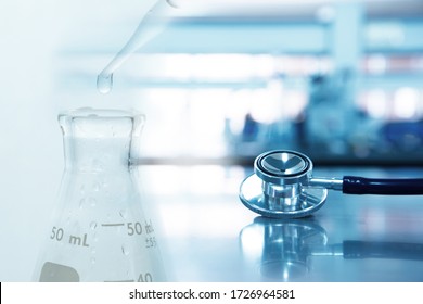 Stethoskop für die ärztliche Diagnose mit Glaskolben mit Wassertropfen auf dem Hintergrund des blauen medizinischen Labors