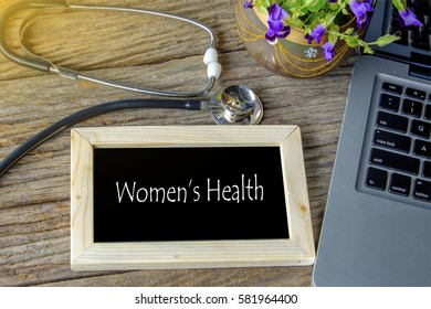 Stethoscope, laptop and flower on wooden table with WOMEN'S HEALTH word as medical concept