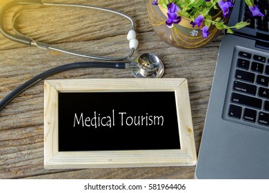 Stethoscope, laptop and flower on wooden table withEDICAL TOURISM word as medical concept