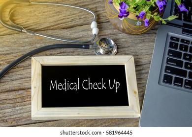 Stethoscope, laptop and flower on wooden table with MEDICAL CHECK UP word as medical concept