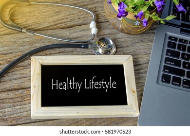 Stethoscope, laptop and flower on wooden table with HEALTHY LIFESTYLE word as medical concept