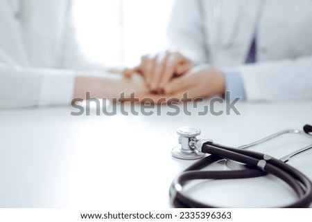 Stethoscope lying on the tablet computer in front of a doctor and patient sitting near each other. Medicine, reassuring hands concept