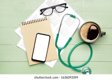 Stethoscope with mobile phone, notebook, document and cup of coffee on table
